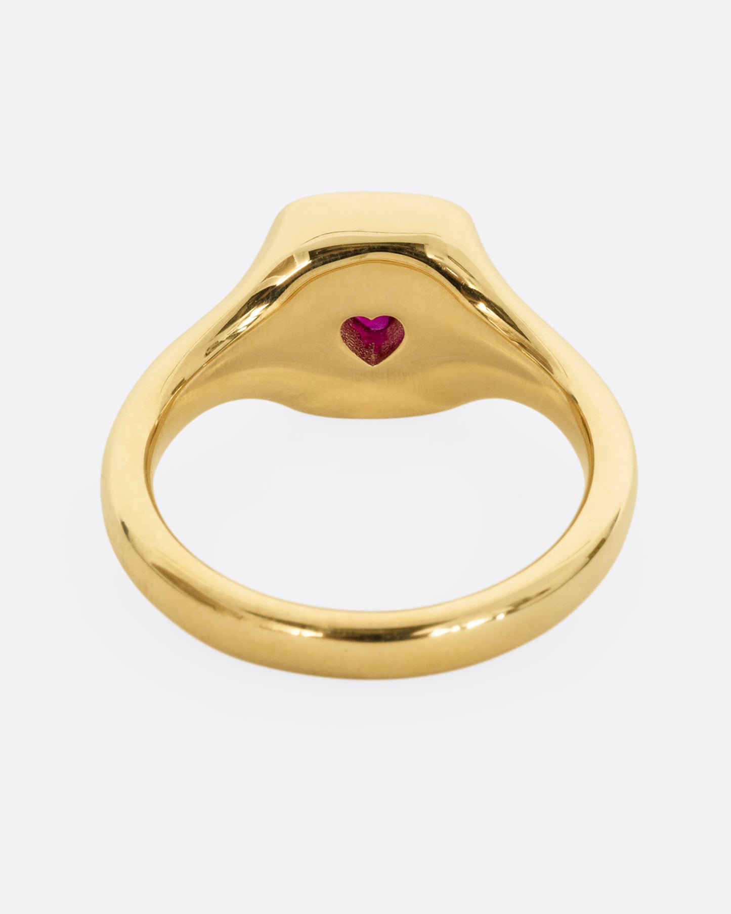 A yellow gold signet ring with cream enamel and a heart shaped ruby. Shown from the back.