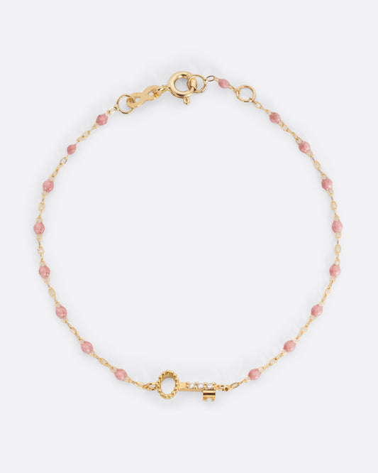 A yellow gold cable chain bracelet with droplets of pink resin and a yellow gold key charm. Three white diamonds are set on the key charm. Shown from the front.