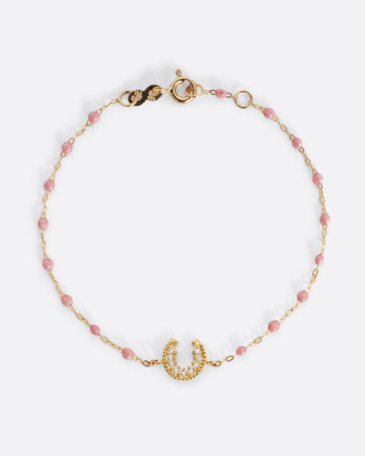 A yellow gold cable chain bracelet with droplets of  pink resin and a diamond lined horseshoe charm. Shown from the front.