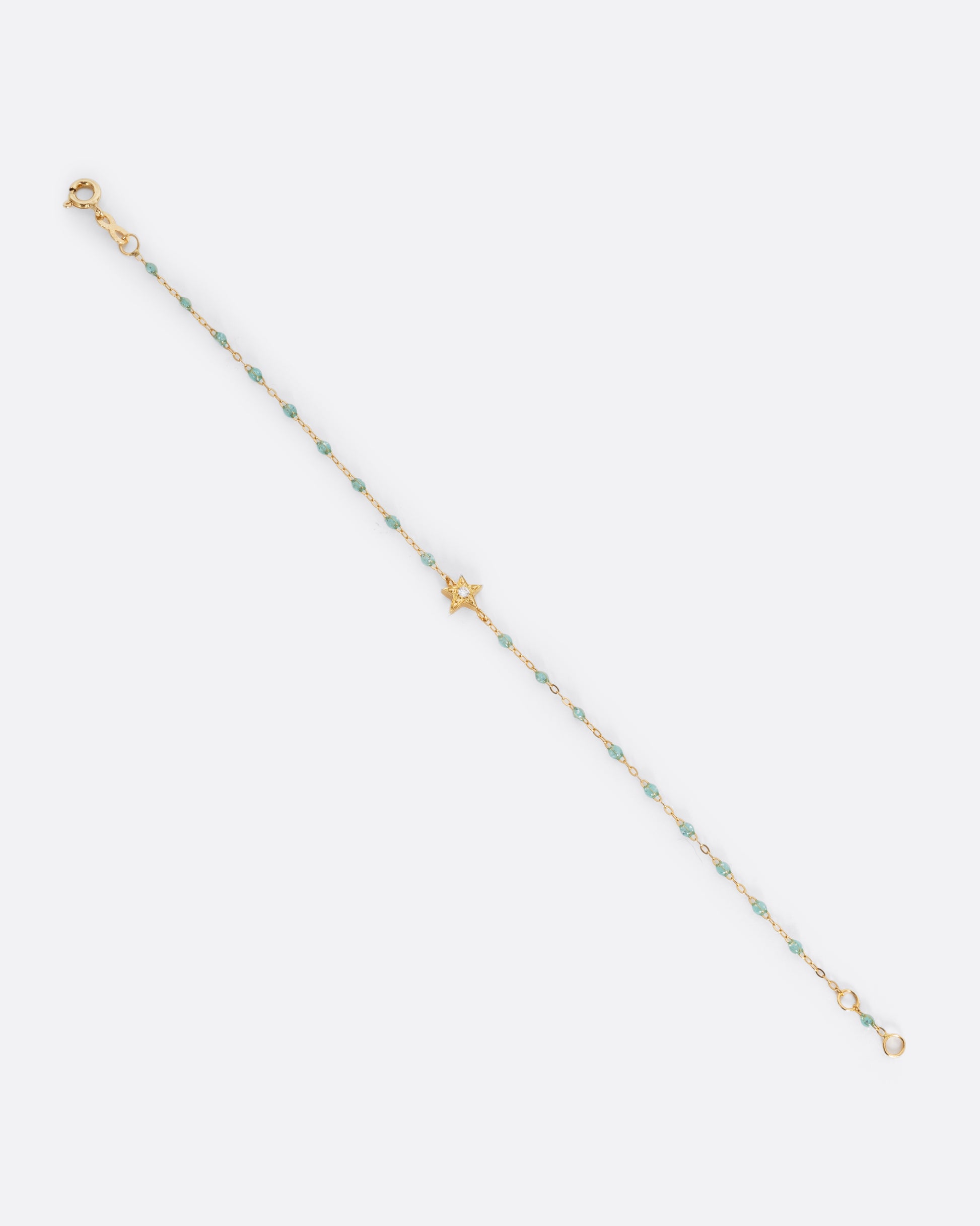A yellow gold cable chain bracelet with droplets of  aqua blue resin and a yellow gold star charm. A single white diamond is set at the center of the star. Shown unclasped from the front.