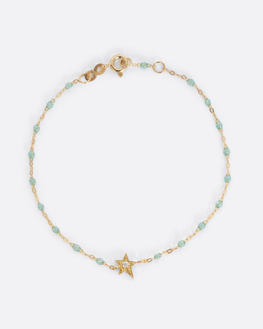 A yellow gold cable chain bracelet with droplets of  aqua blue resin and a yellow gold star charm. A single white diamond is set at the center of the star. Shown from the front.