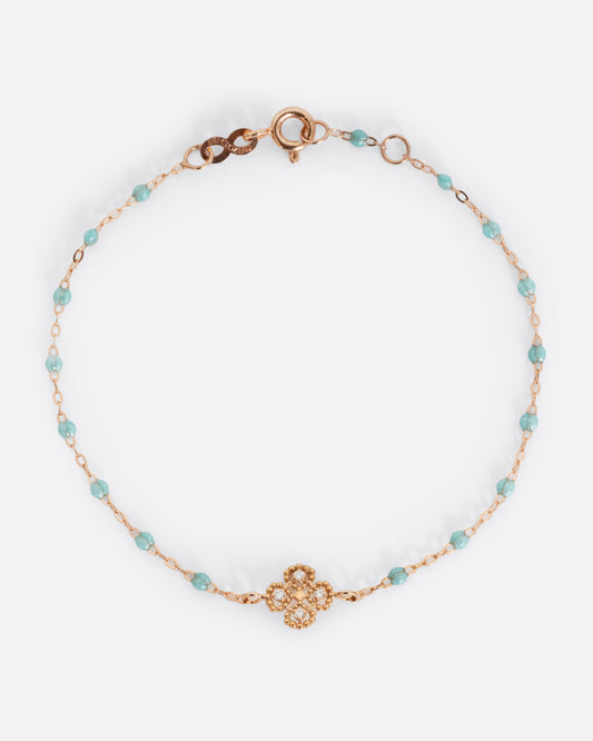 A yellow gold cable chain bracelet with droplets of clear blue resin and a yellow gold clover charm. Four diamonds are set on the clover charm. Shown from the front.