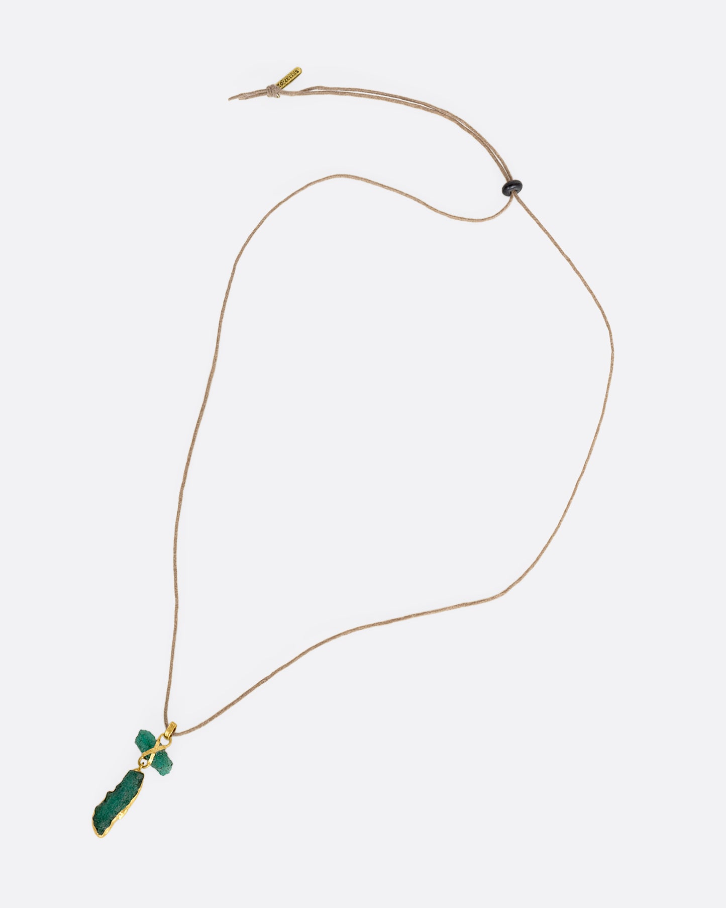 A high karat yellow gold necklace with an two raw emeralds on a cord. Shown laying flat.