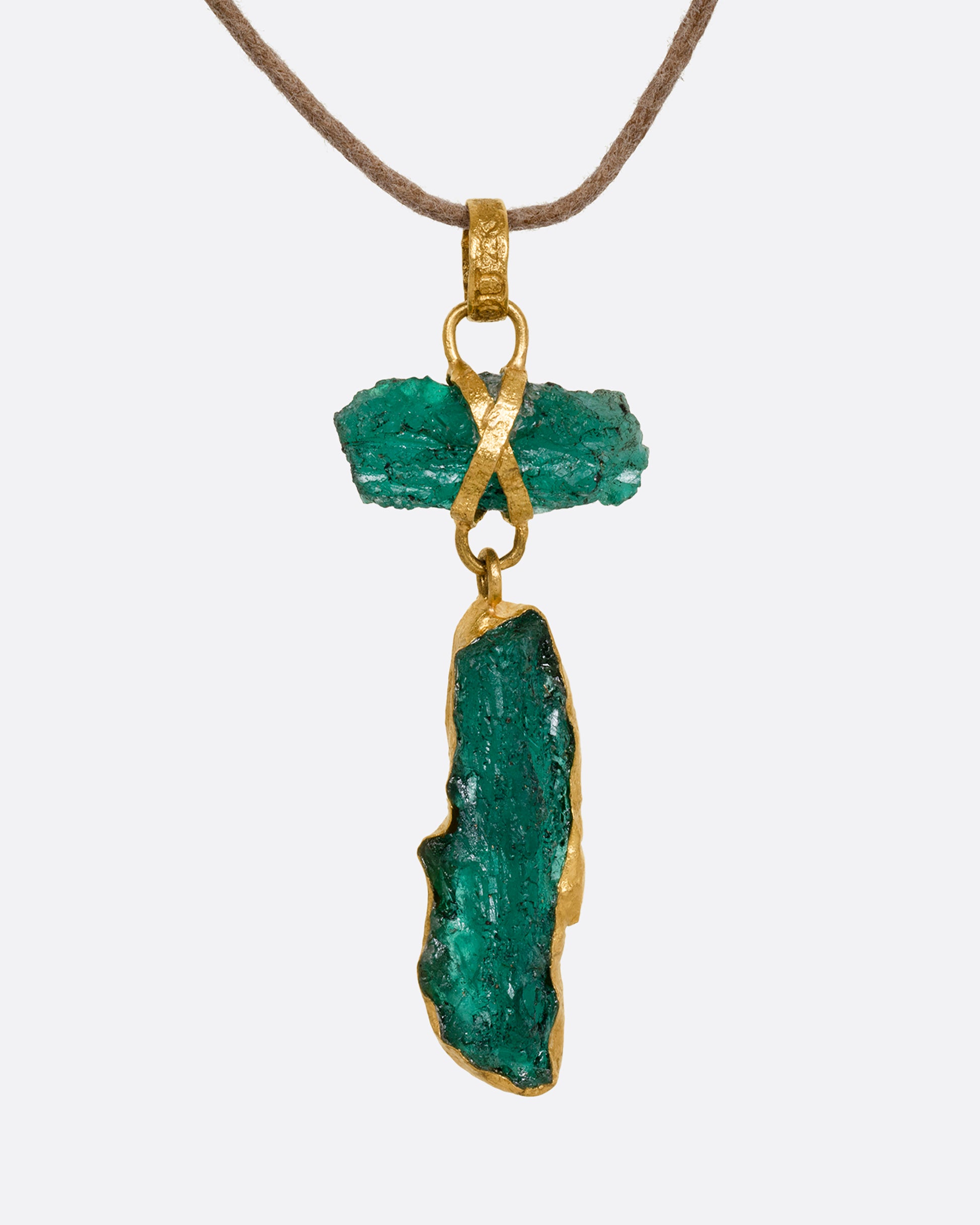 A high karat yellow gold necklace with an two raw emeralds on a cord. Shown from the front.