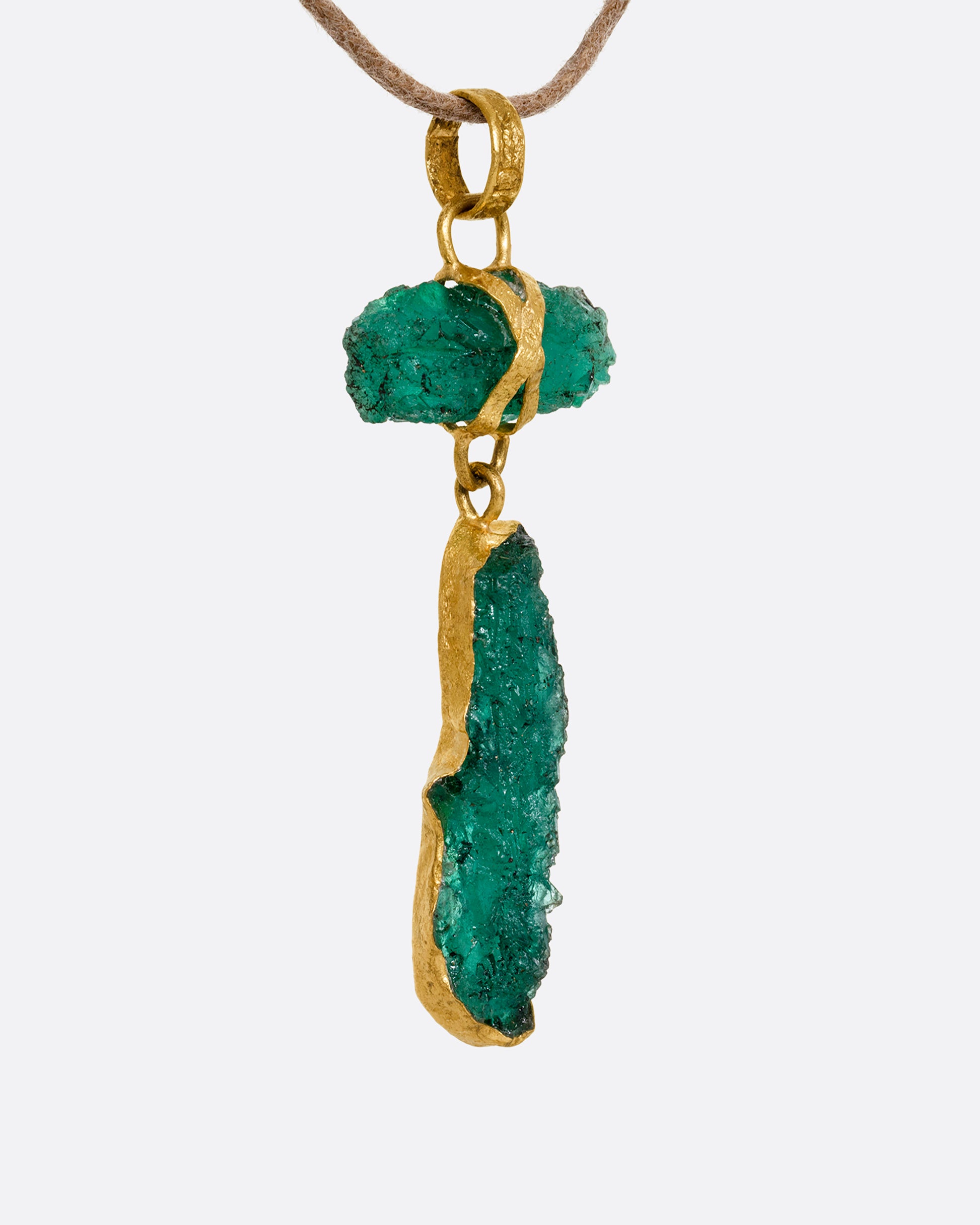 A high karat yellow gold necklace with an two raw emeralds on a cord. Shown from the side.