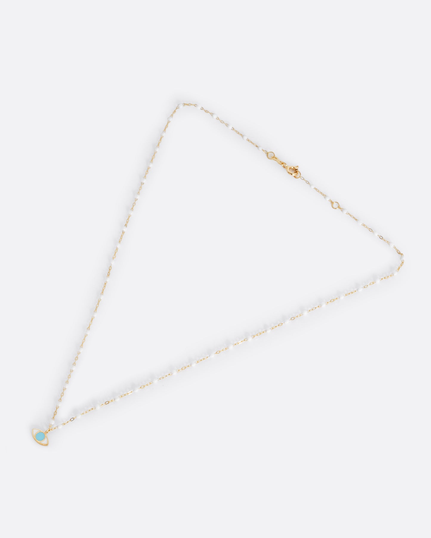 A yellow gold cable chain necklace with droplets of white resin and an eye charm. The iris of the eye charm is turquoise blue enamel and the sclera is white. Shown from the front.