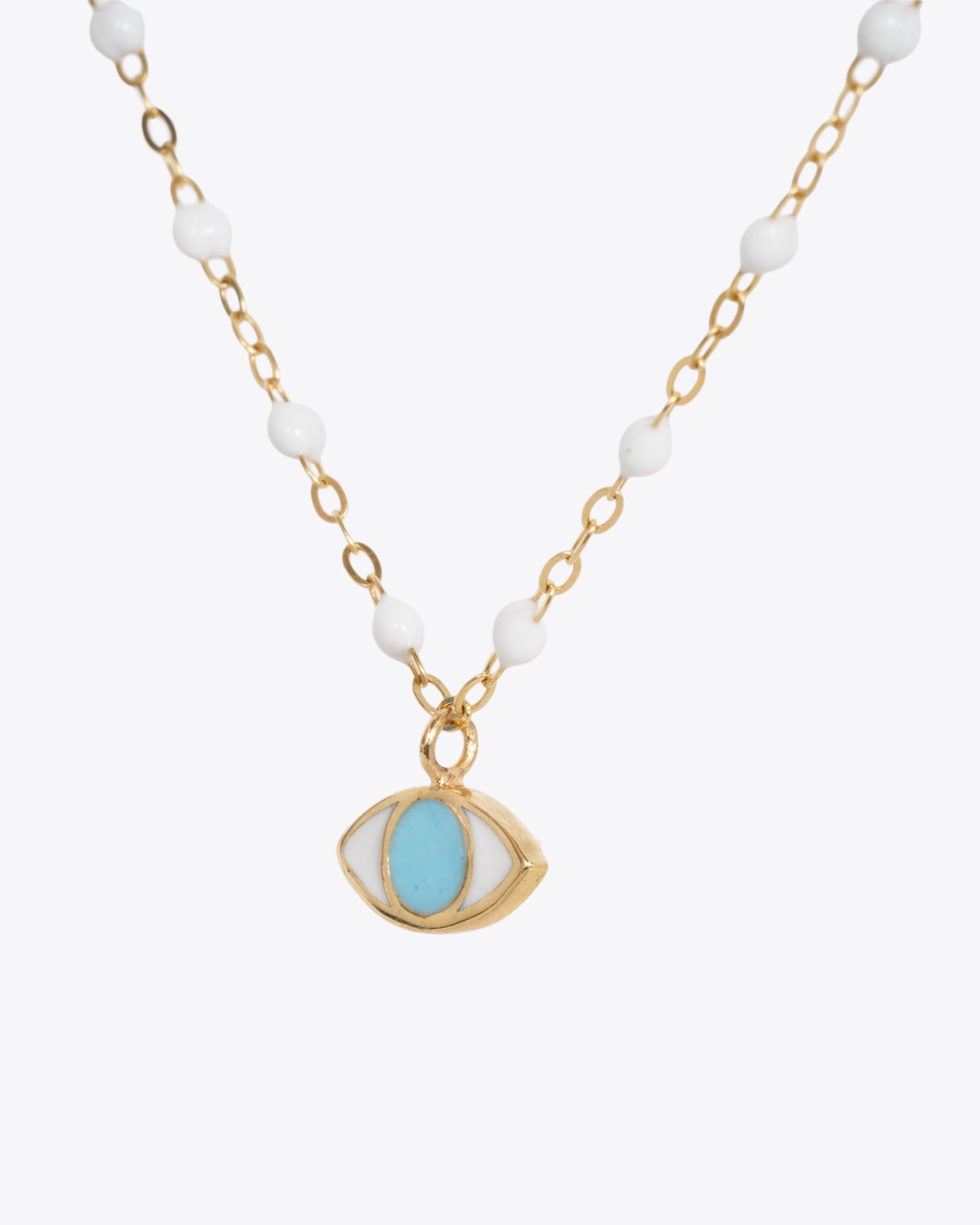 A close up shot of a yellow gold cable chain necklace with droplets of white resin and an eye charm. The iris of the eye charm is turquoise blue enamel and the sclera is white. Shown from the side.