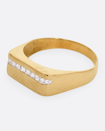 A yellow gold signet ring with a queue of Asscher cut diamonds stretching across the face. Shown from the side.