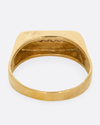 A yellow gold signet ring with a queue of Asscher cut diamonds stretching across the face. Shown from the back.