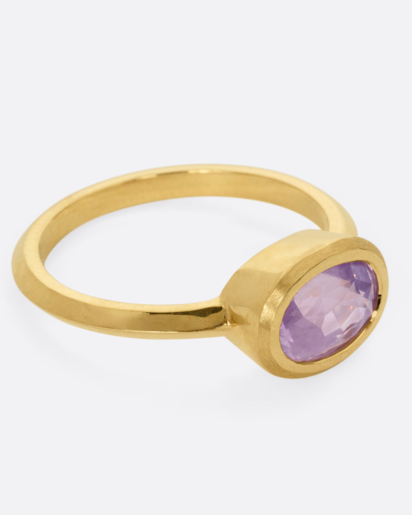 A yellow gold ring with a lilac sapphire, shown from the side.