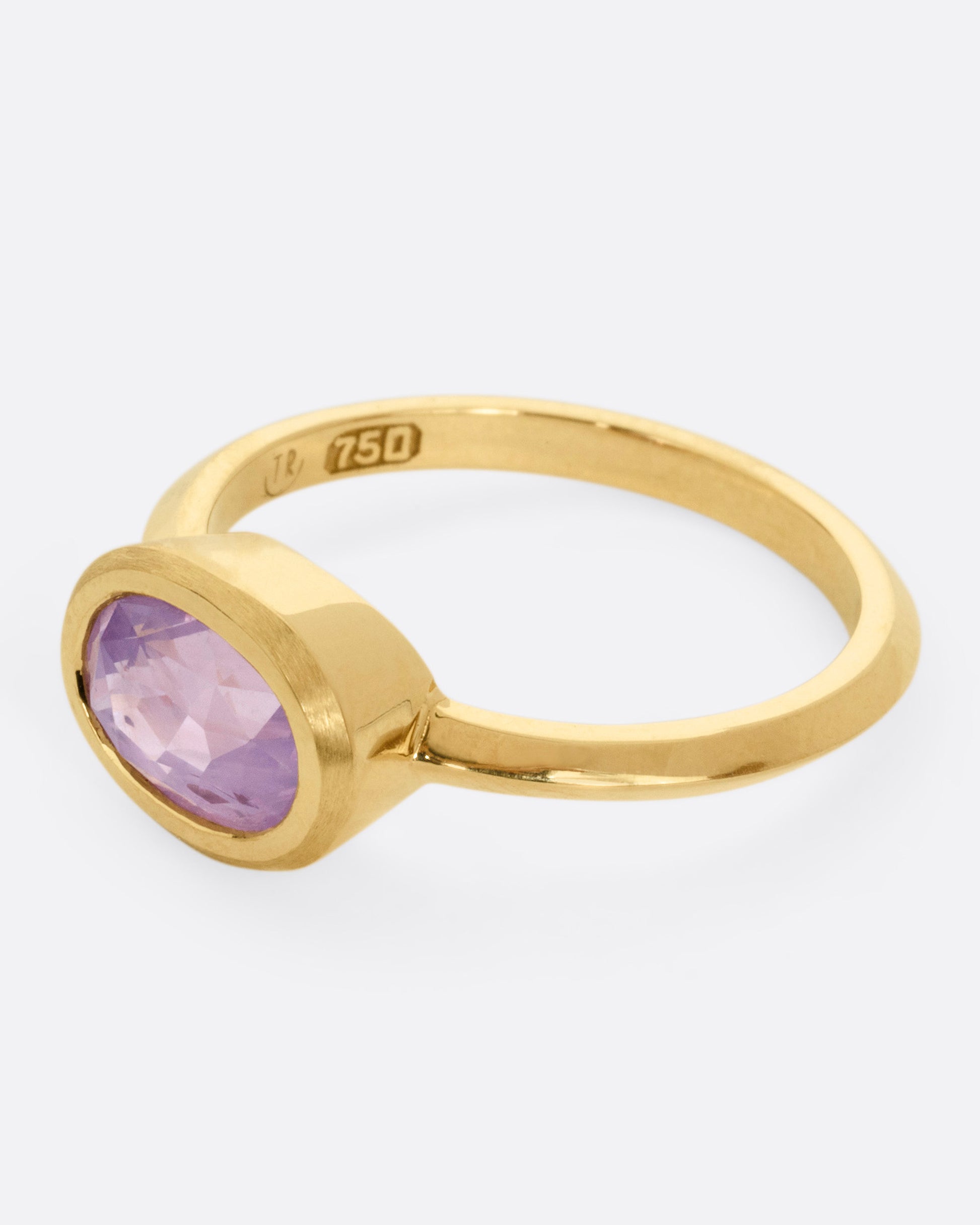 A yellow gold ring with a lilac sapphire, shown from the side.