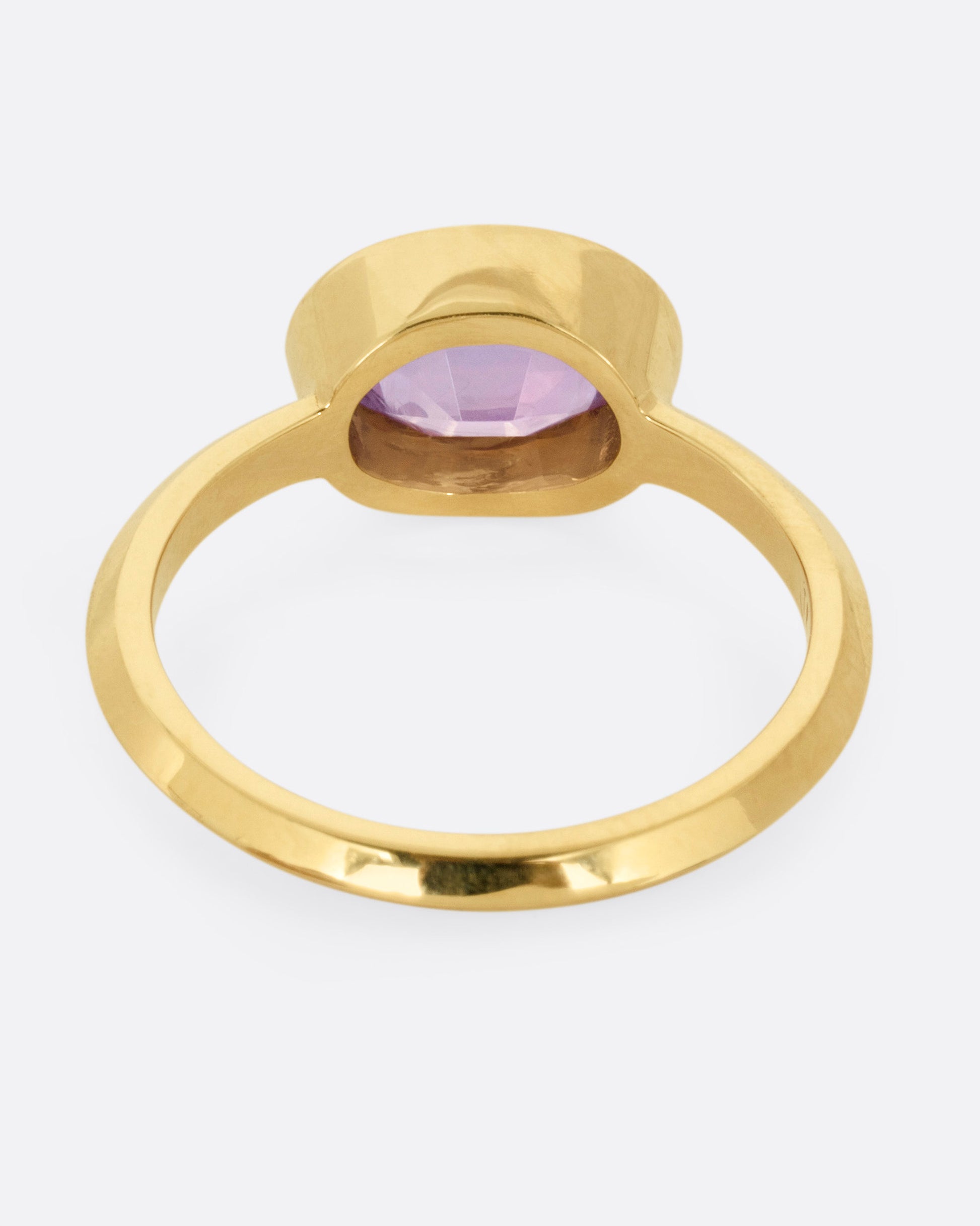 A yellow gold ring with a lilac sapphire, shown from the back.
