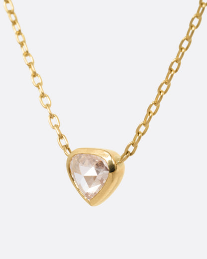 A yellow gold necklace with a natural organic heart shaped diamond, shown from the side.