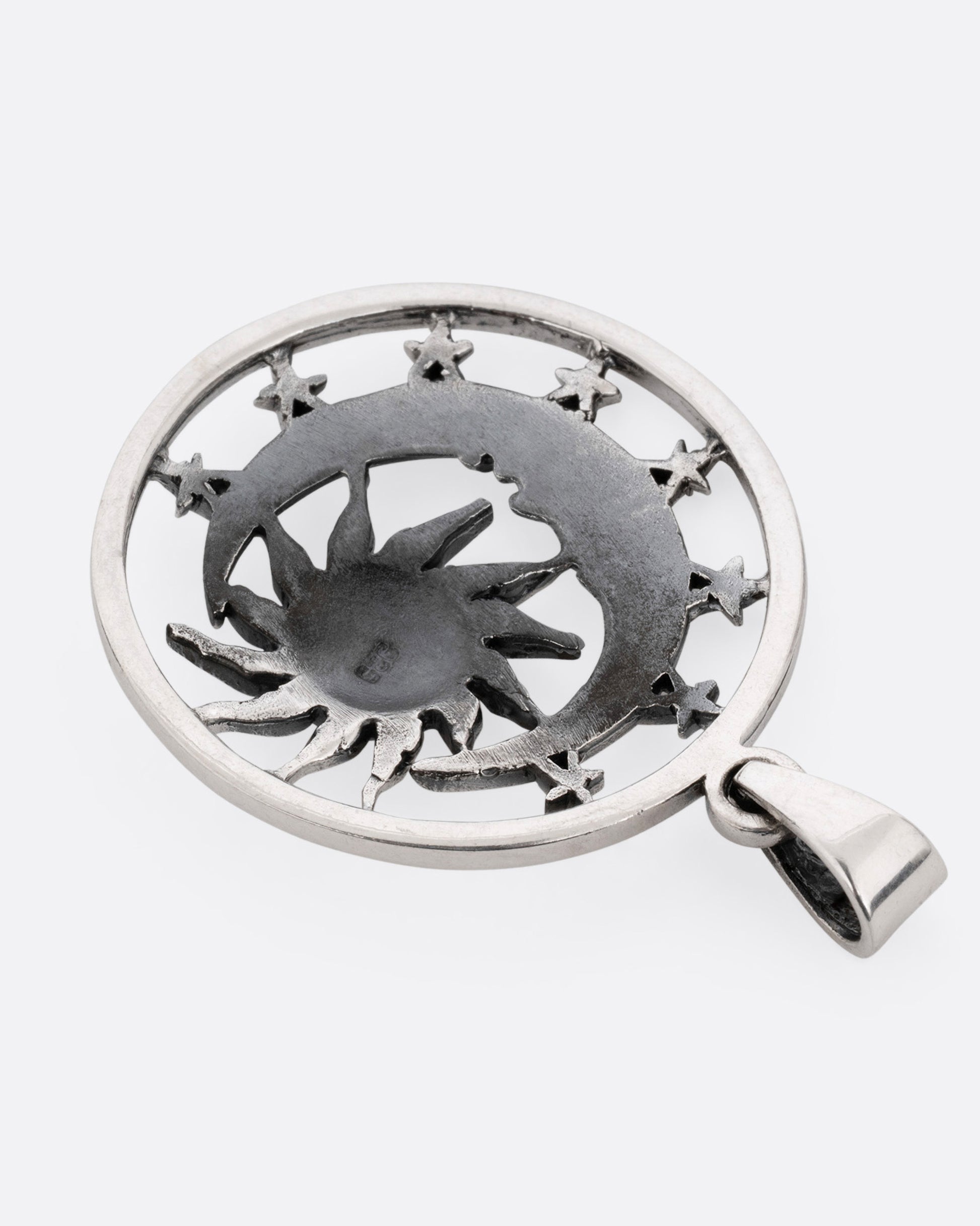 A circular silver pendant with the sun, moon, and stars, shown from the back.