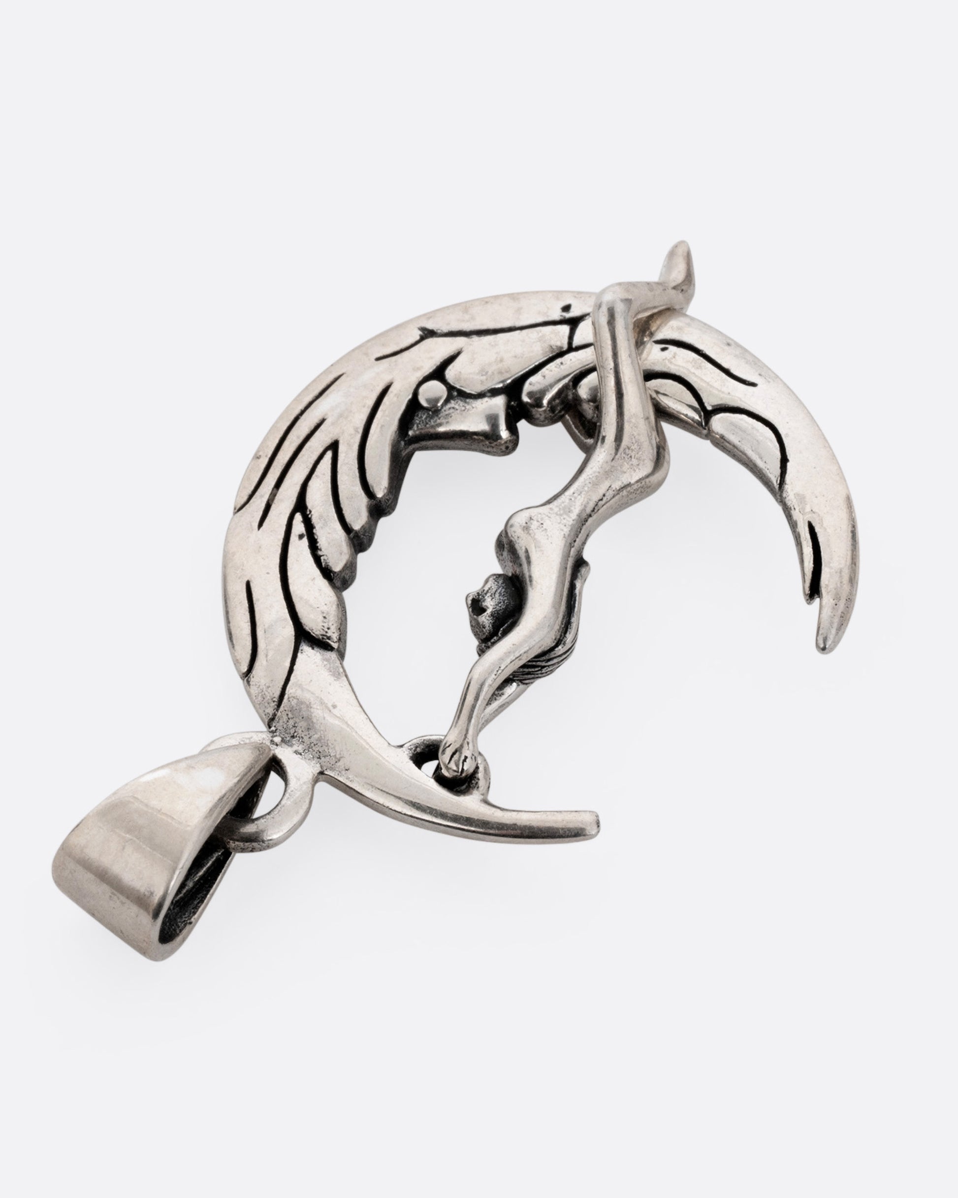 A silver pendant with a woman grasping a craggy crescent moon, shown from the back.