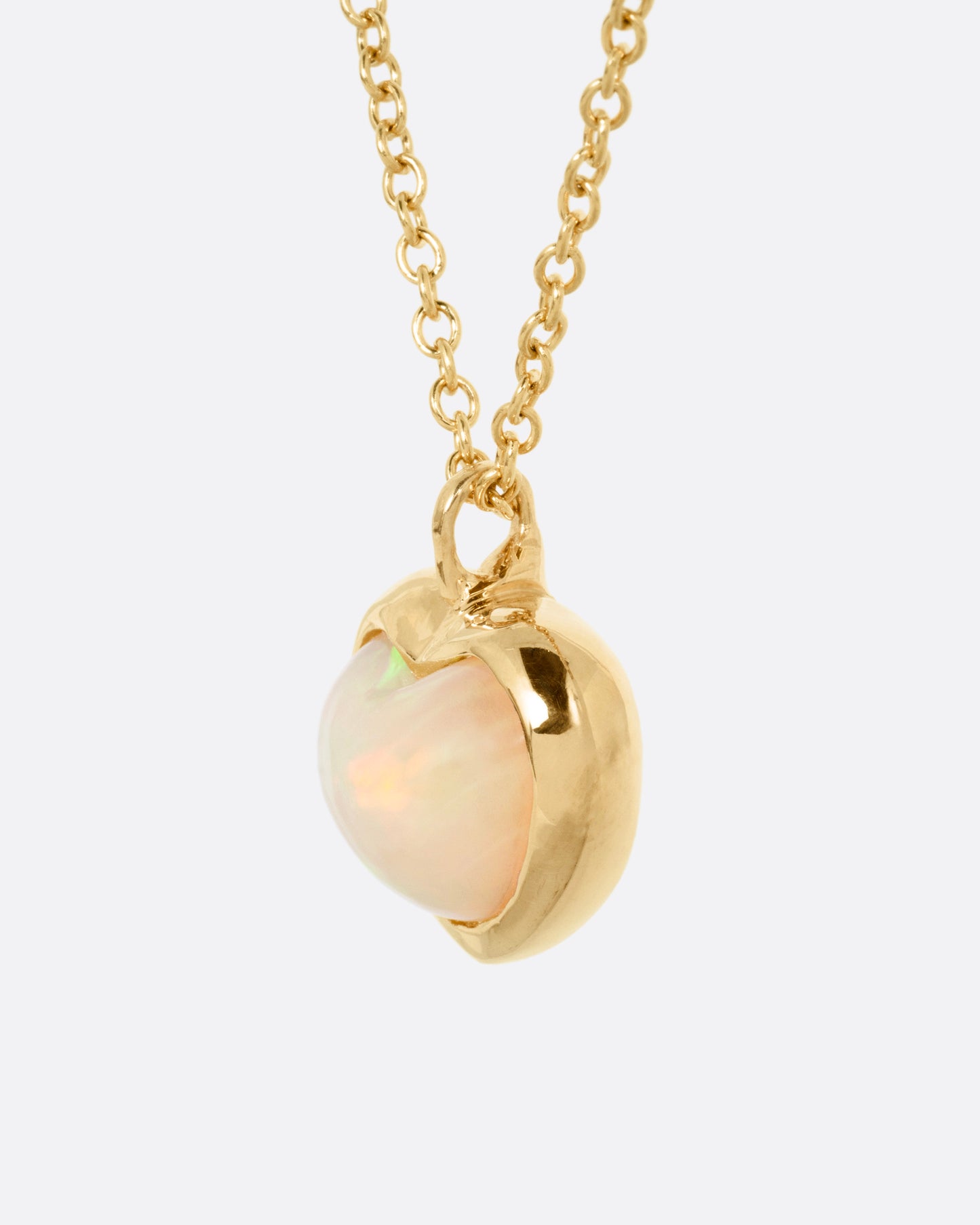 A yellow gold cable chain necklace with a large dimensional opal heart pendant, shown from the side.