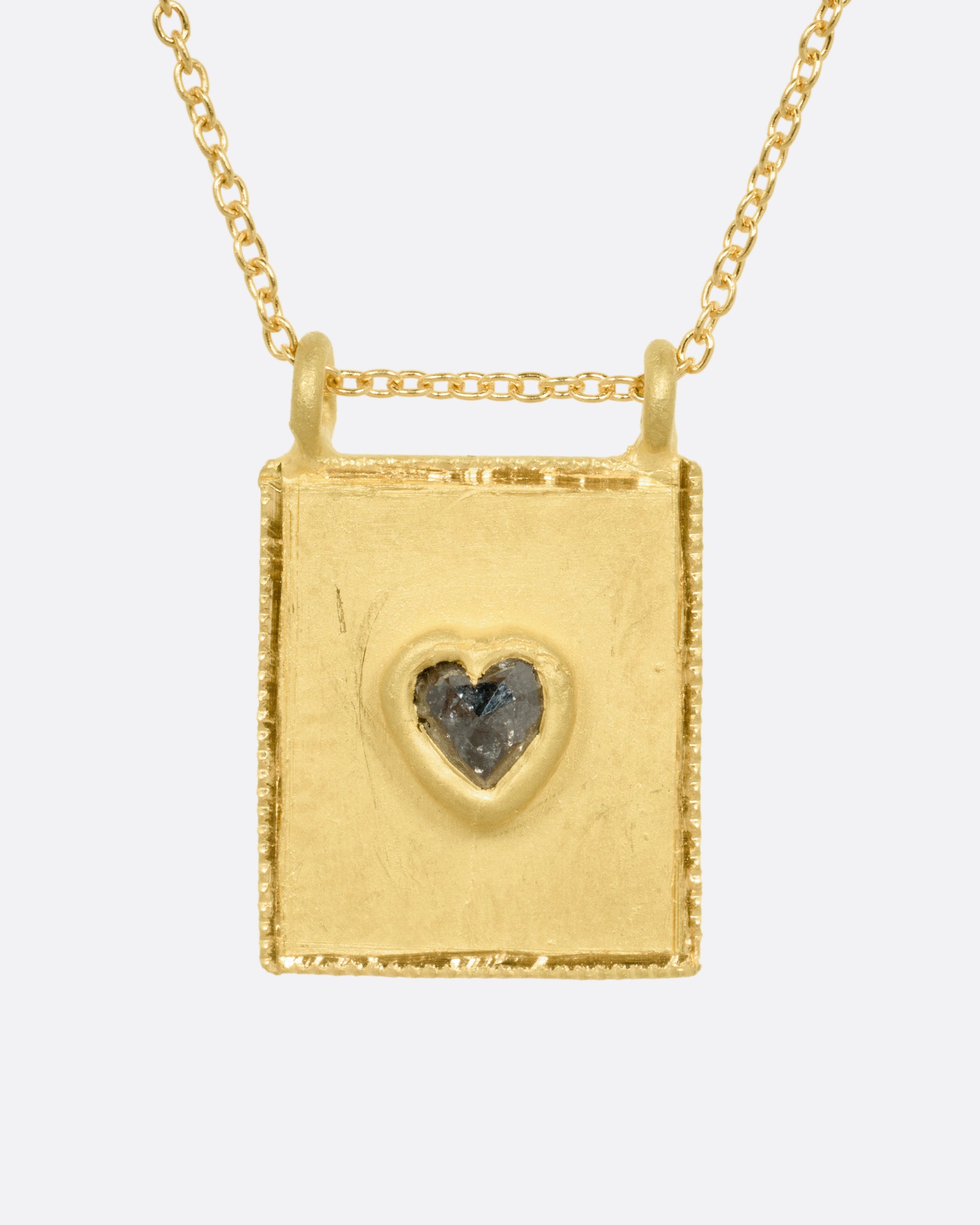 A yellow gold pendant necklace with a heart shaped salt and pepper diamond in a rectangular gold frame, with a double bail. Shown from the front.