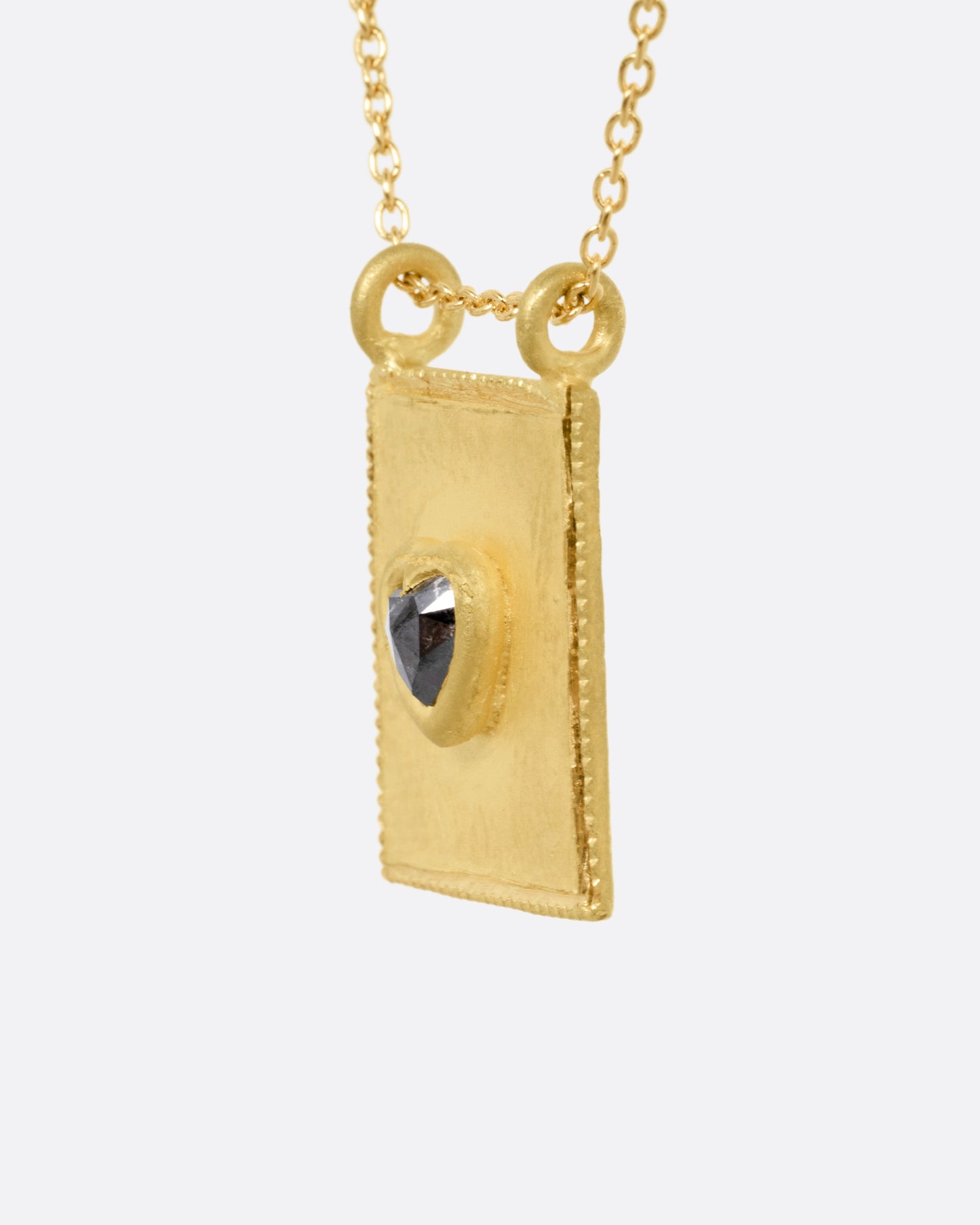 A yellow gold pendant necklace with a heart shaped salt and pepper diamond in a rectangular gold frame, with a double bail. Shown from the side.