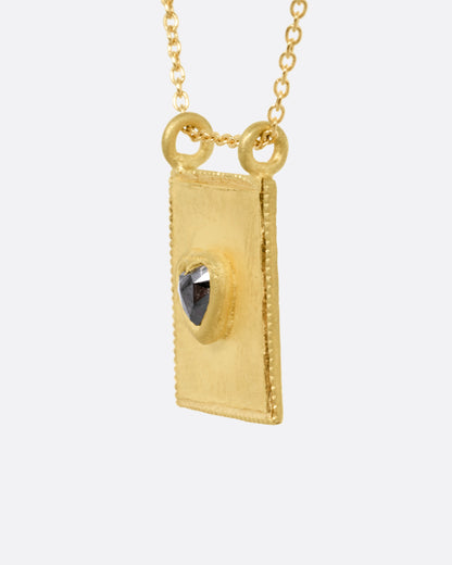 A yellow gold pendant necklace with a heart shaped salt and pepper diamond in a rectangular gold frame, with a double bail. Shown from the side.