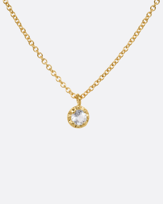 A yellow gold cable chain necklace with a  prong set aquamarine, shown from the front.