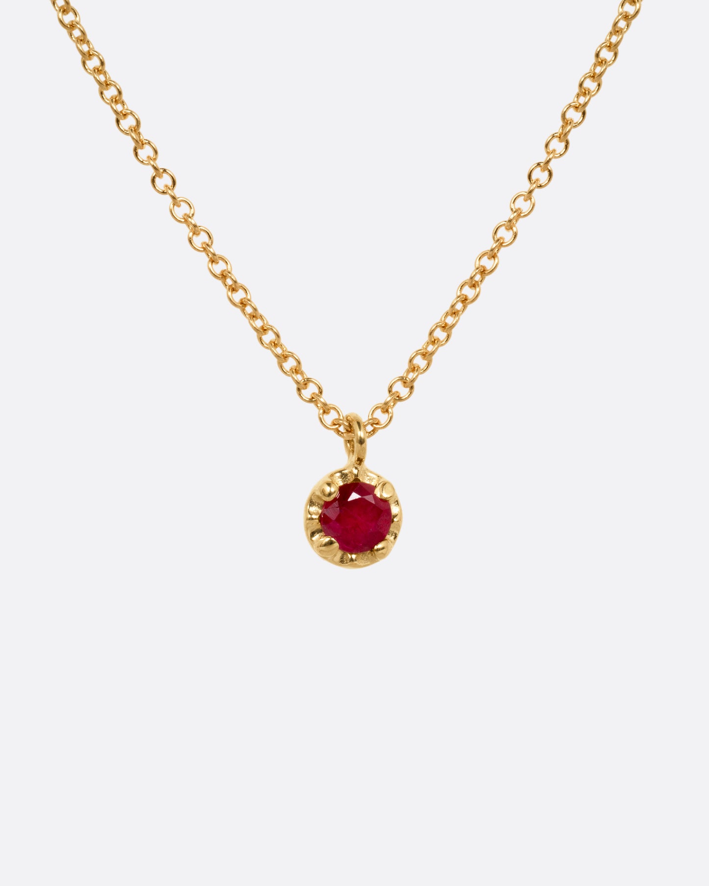 A yellow gold cable chain necklace with a  prong set ruby, shown from the front.