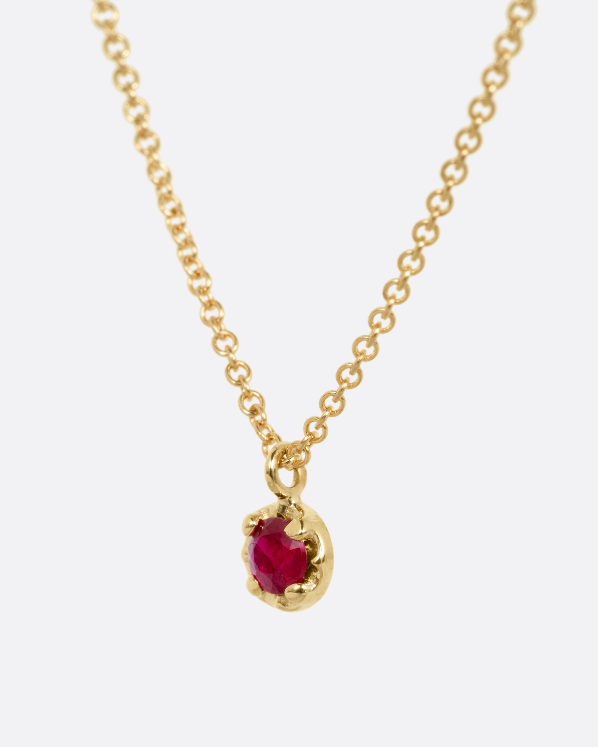 A yellow gold cable chain necklace with a  prong set ruby, shown from the side.