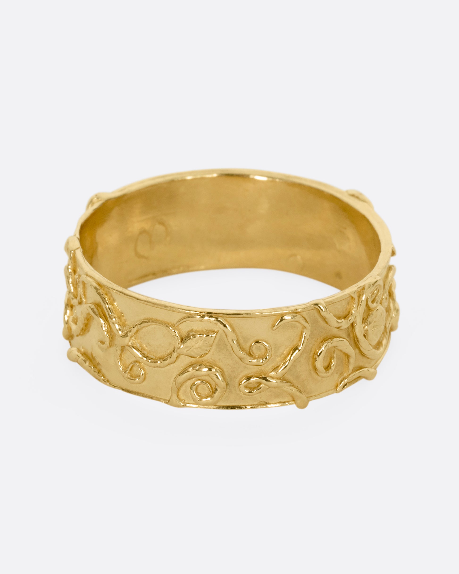 A yellow gold band ring wreathed in vines and leaves. Shown from the front.