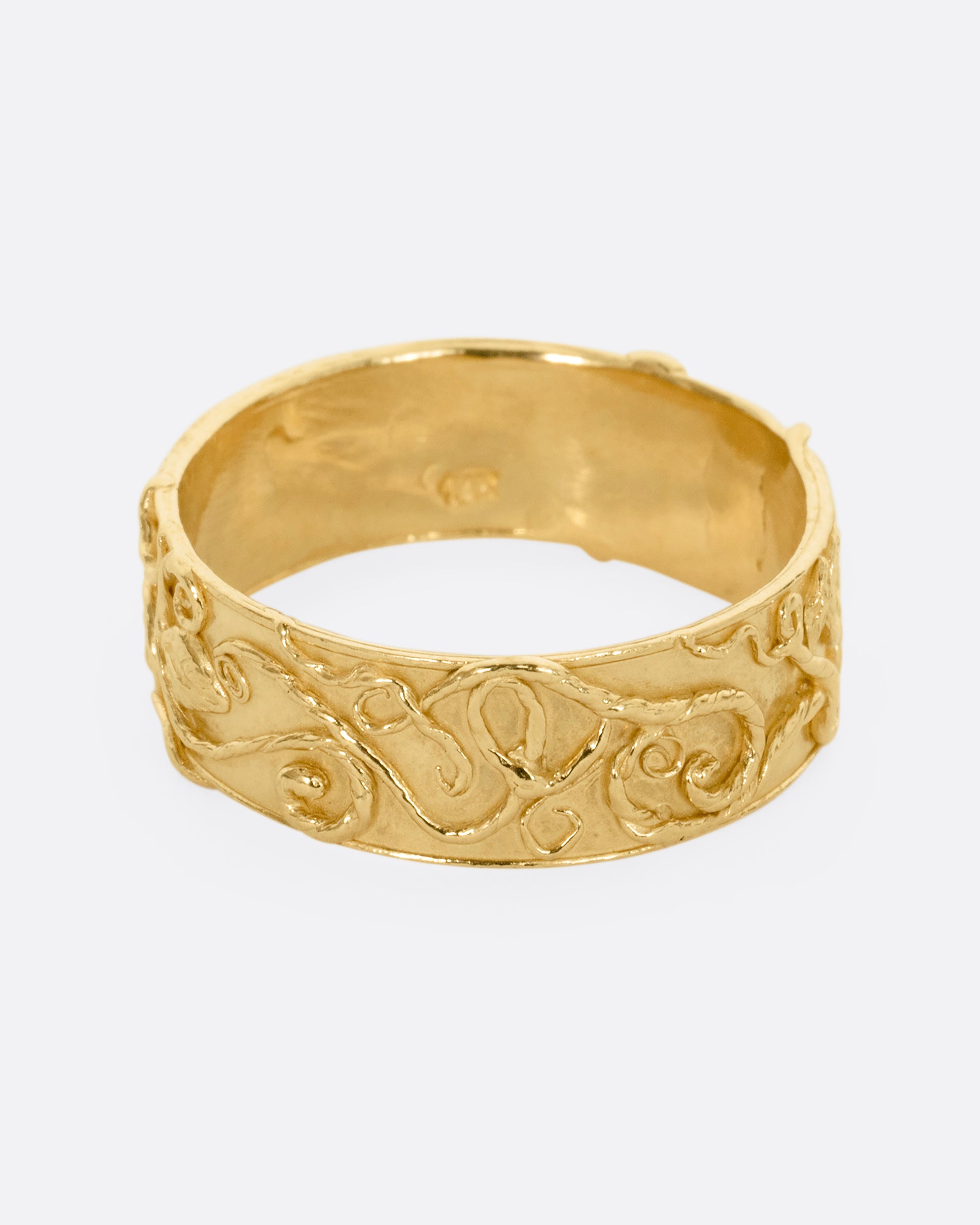 A yellow gold band ring wreathed in vines and leaves. Shown from the front.