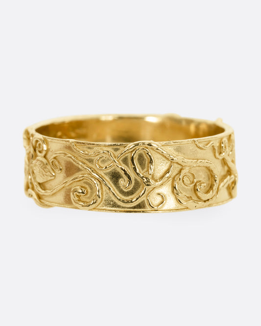 A yellow gold band ring wreathed in vines and leaves. Shown from the front.