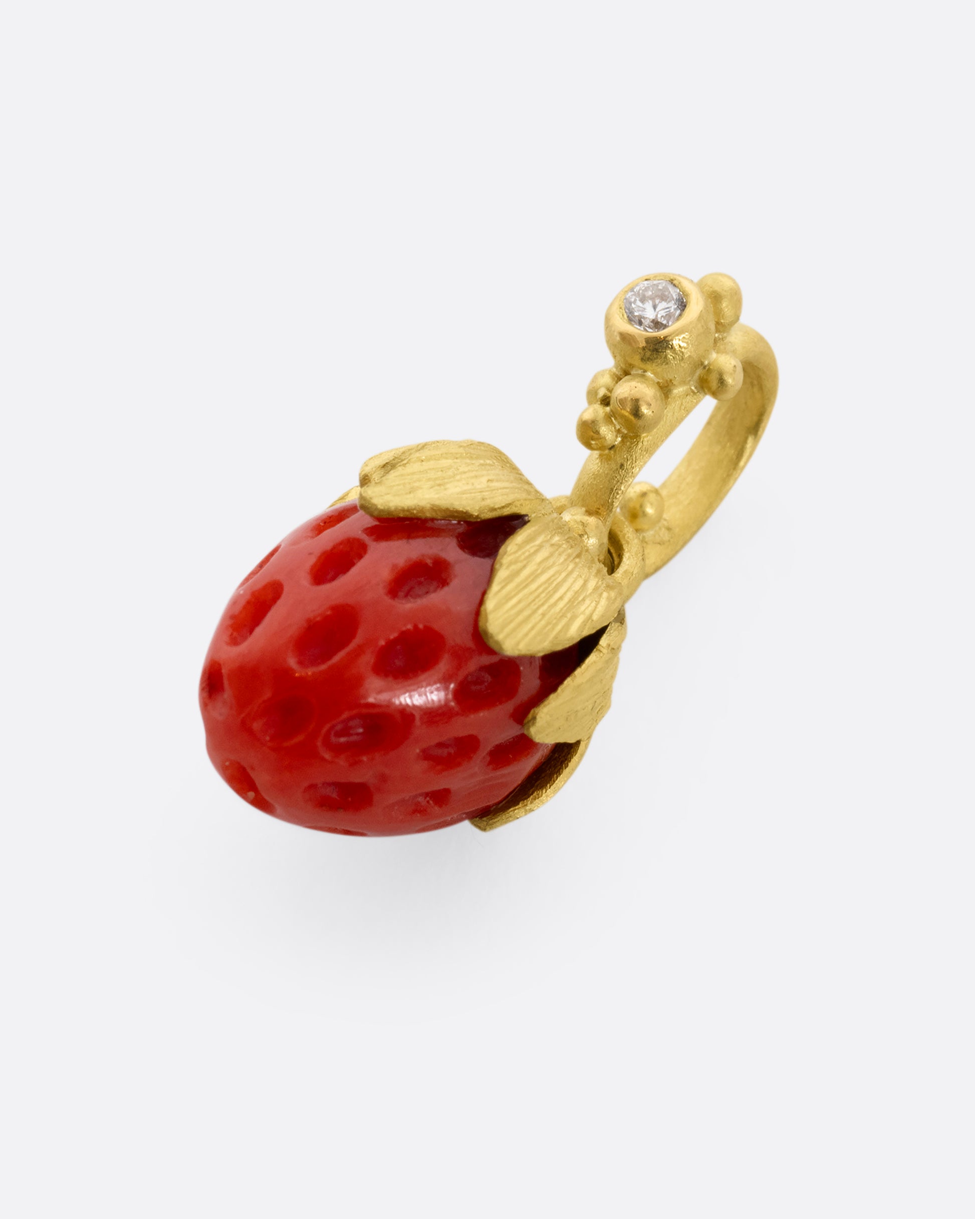 yellow gold charm with diamond and strawberry shaped coral shown lying flat
