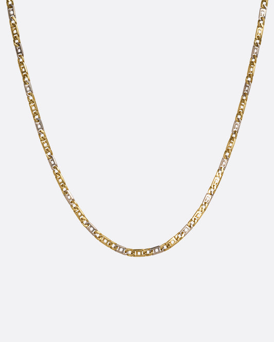 A white and yellow gold geometric flat chain necklace. Shown hanging from the front.