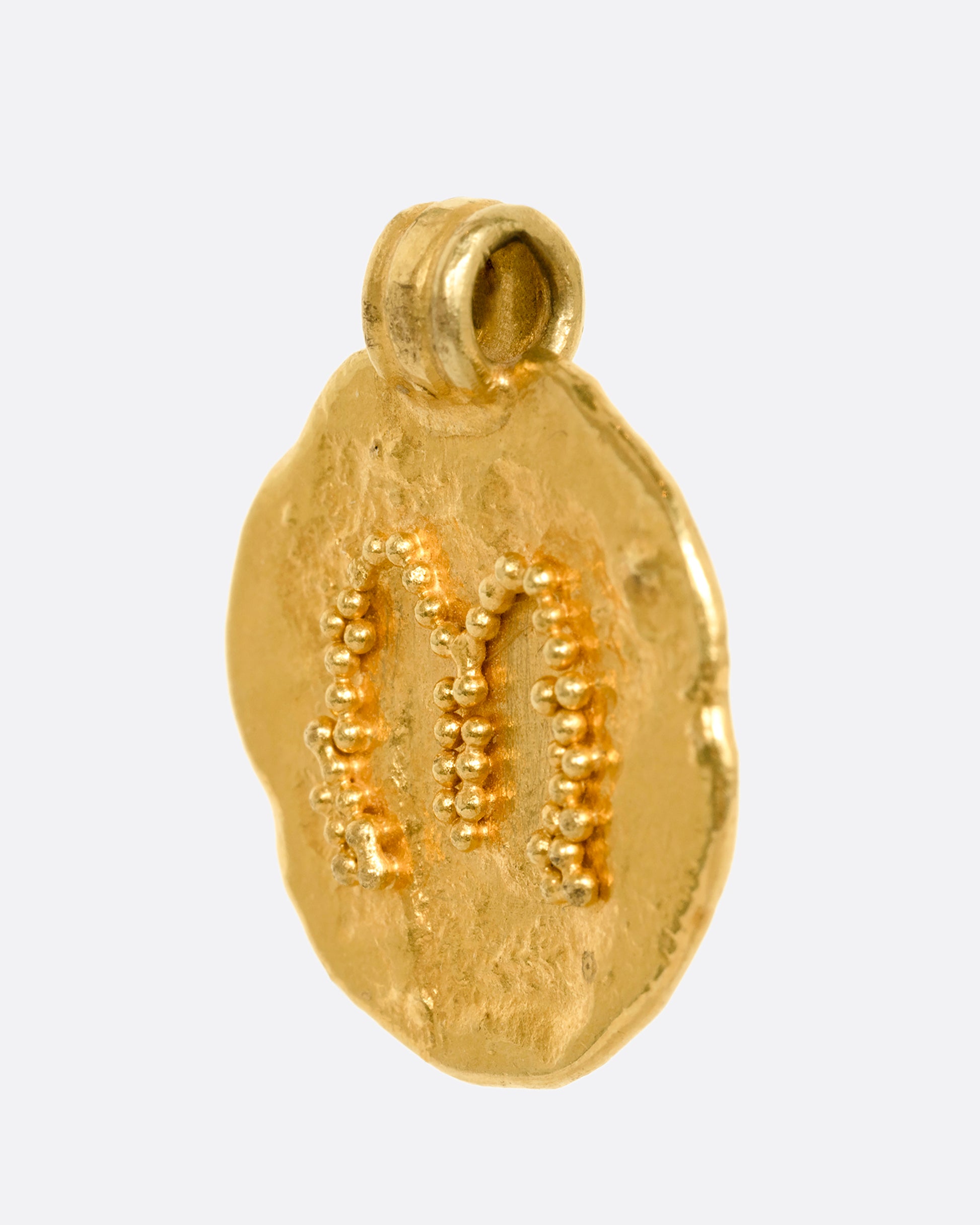 A high carat yellow gold organic circle pendant with the letter m on the face. Shown from the side.