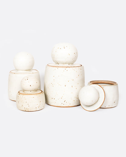 A group of white stoneware jars with lids with ball shaped tops. Shown from the front.