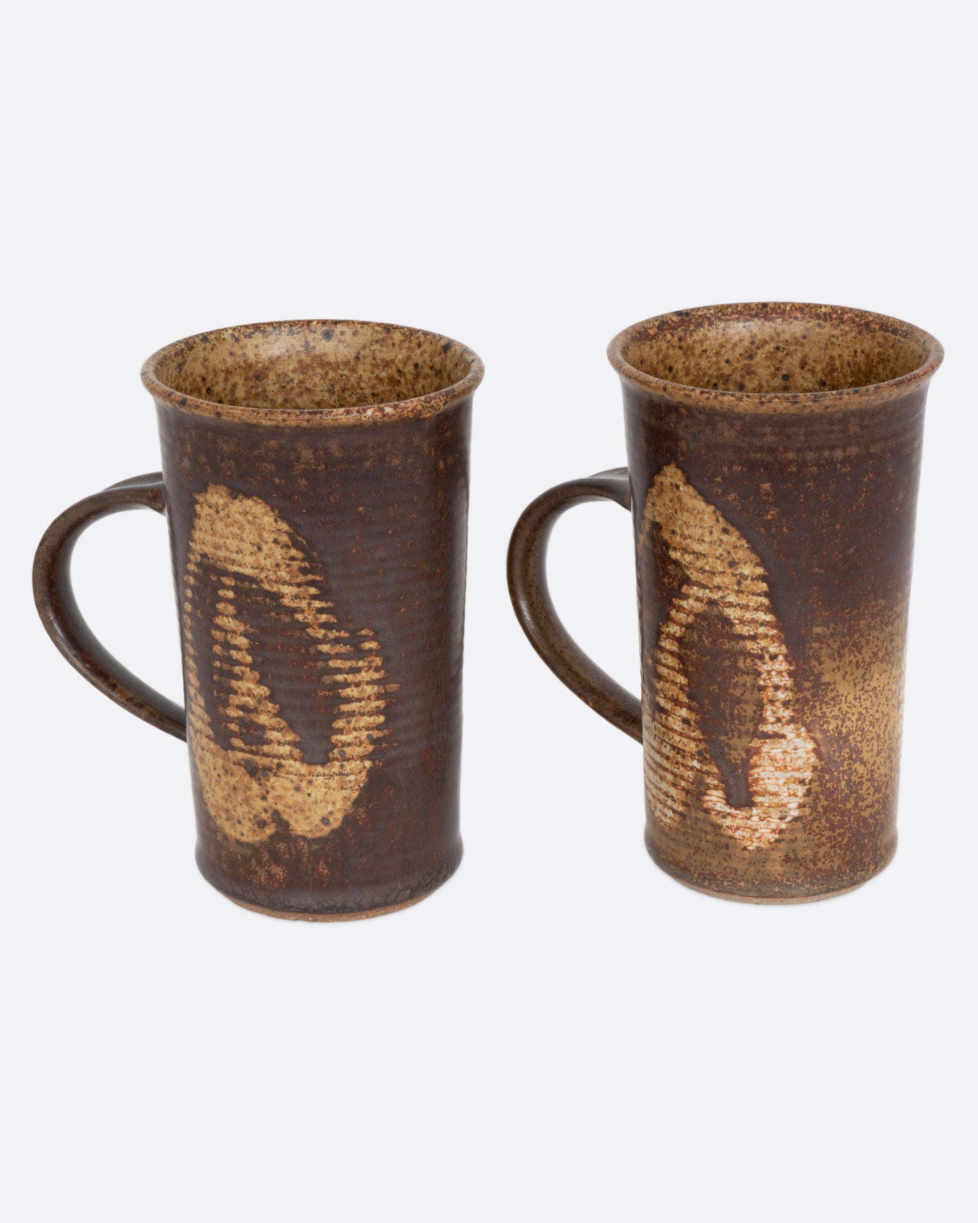 A pair of brown mugs with a ribbed texture and dynamic abstract glaze, shown from the side.