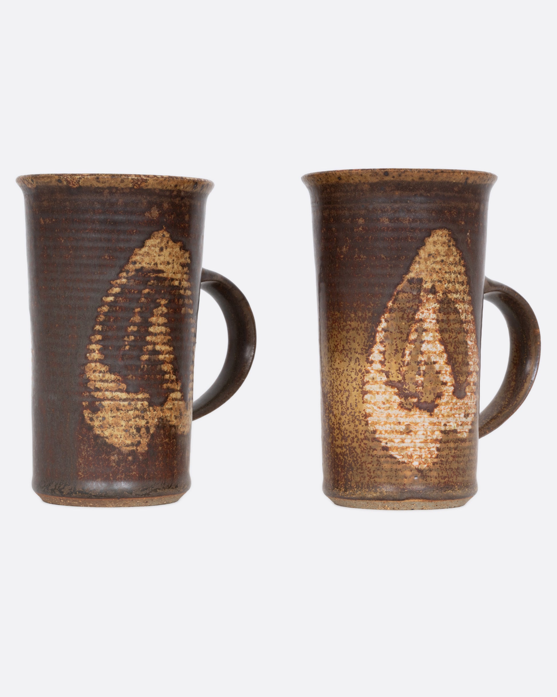 A pair of brown mugs with a ribbed texture and dynamic abstract glaze, shown from the side.