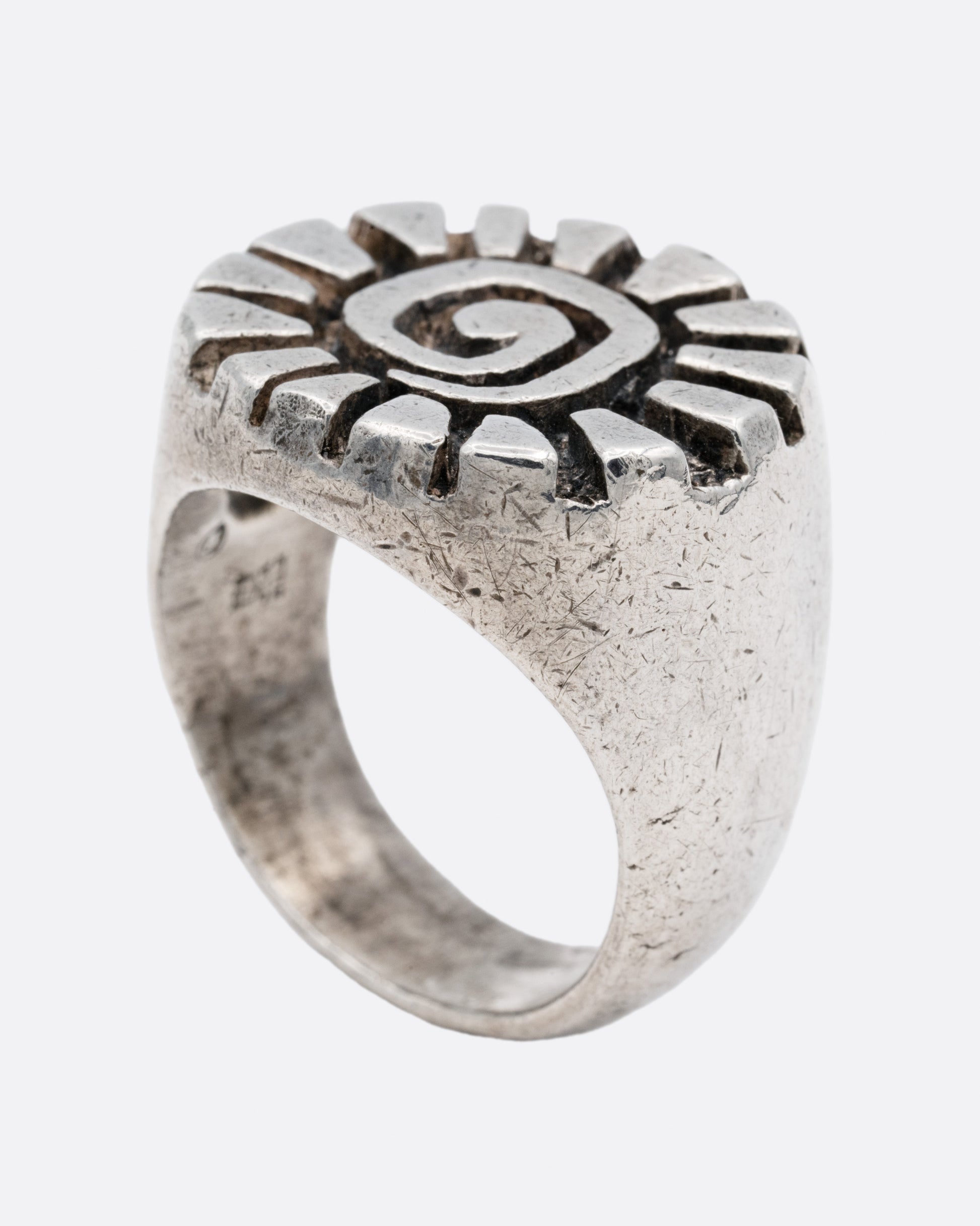 A silver ring with a graphic spiral sun, shown from the side standing up.