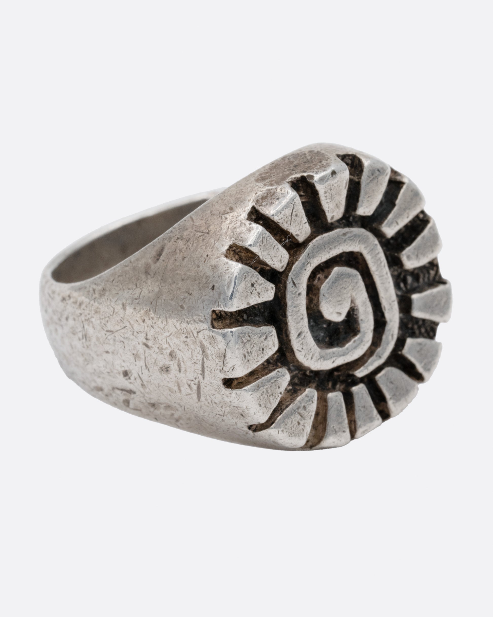 A silver ring with a graphic spiral sun, shown from the side.