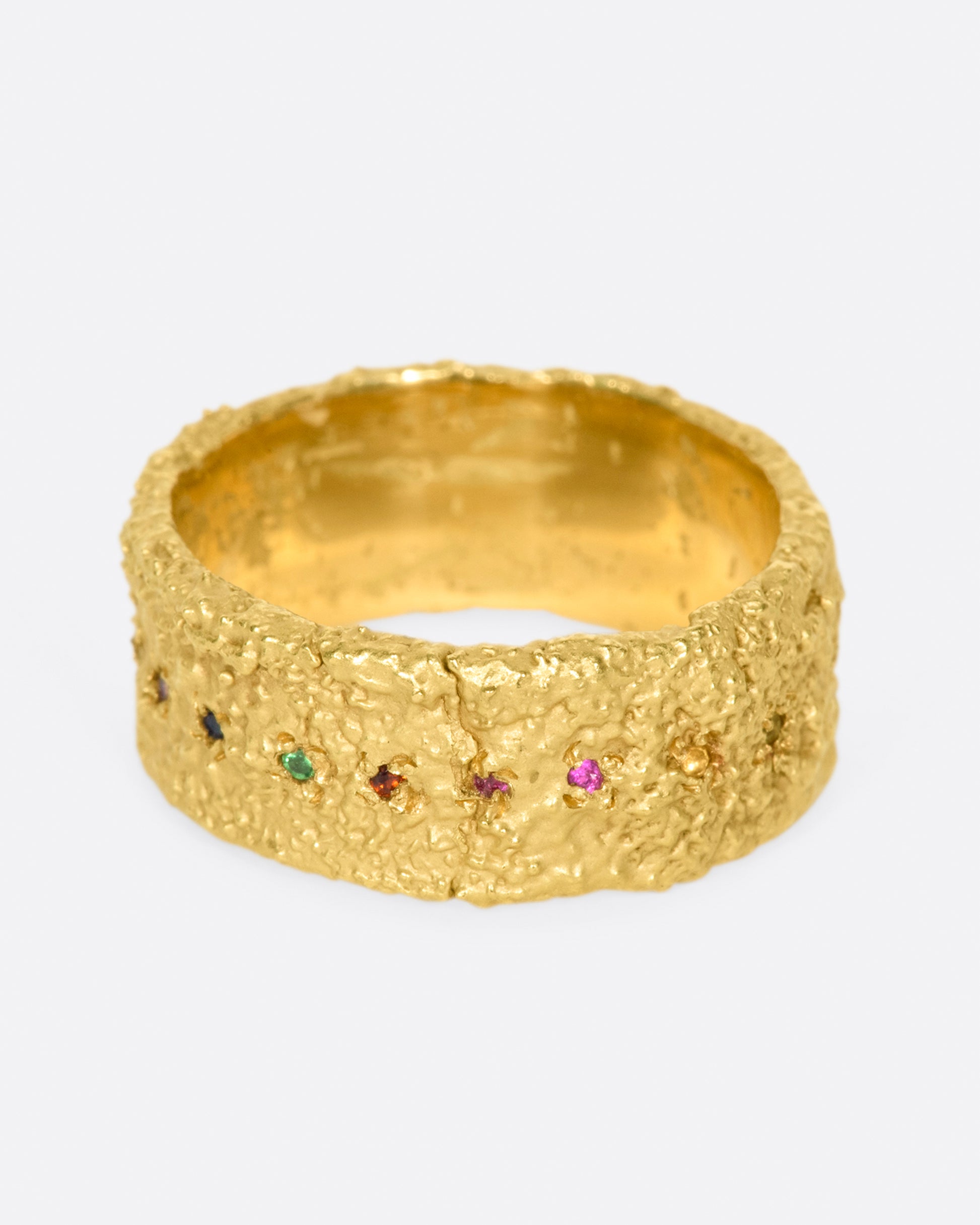 A wide textured band made with recycled yellow gold set with garnet, ruby, peridot, aquamarine, amethyst, emerald, and pink, orange, yellow and blue sapphires.