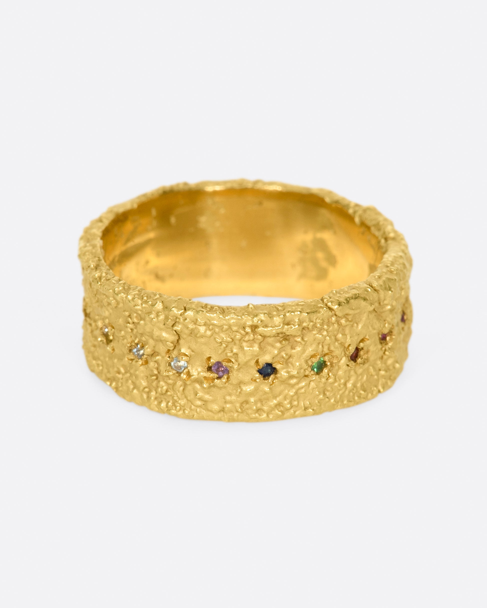 A wide textured band made with recycled yellow gold set with garnet, ruby, peridot, aquamarine, amethyst, emerald, and pink, orange, yellow and blue sapphires.