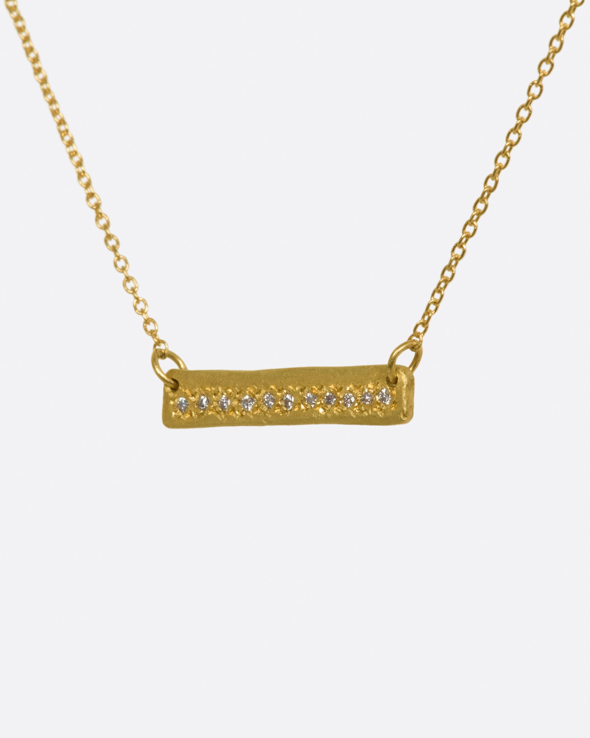 A yellow gold bar necklace with a single row of white diamonds. View from the side.