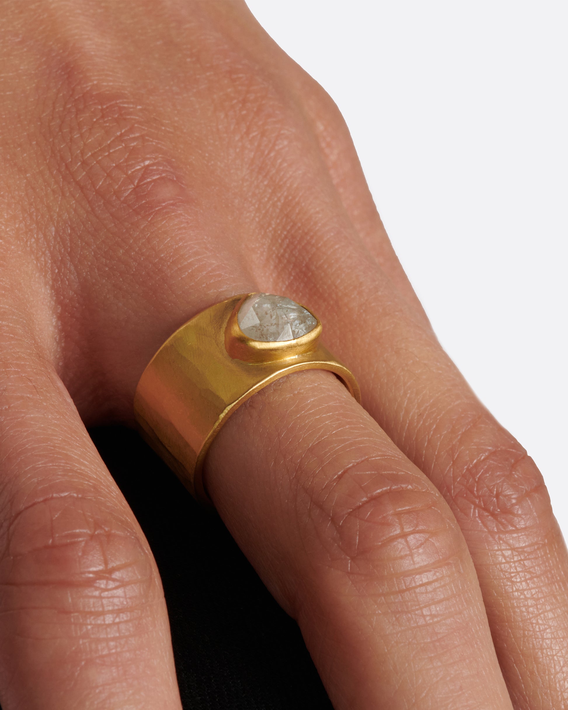 A wide, matte, hammered band with a rose cut gray diamond embedded in a high karat gold setting.