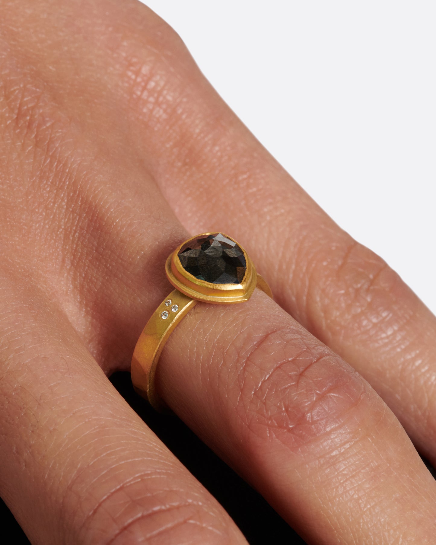 A faceted, pear shaped black diamond in a 22k gold setting with white diamond accents.