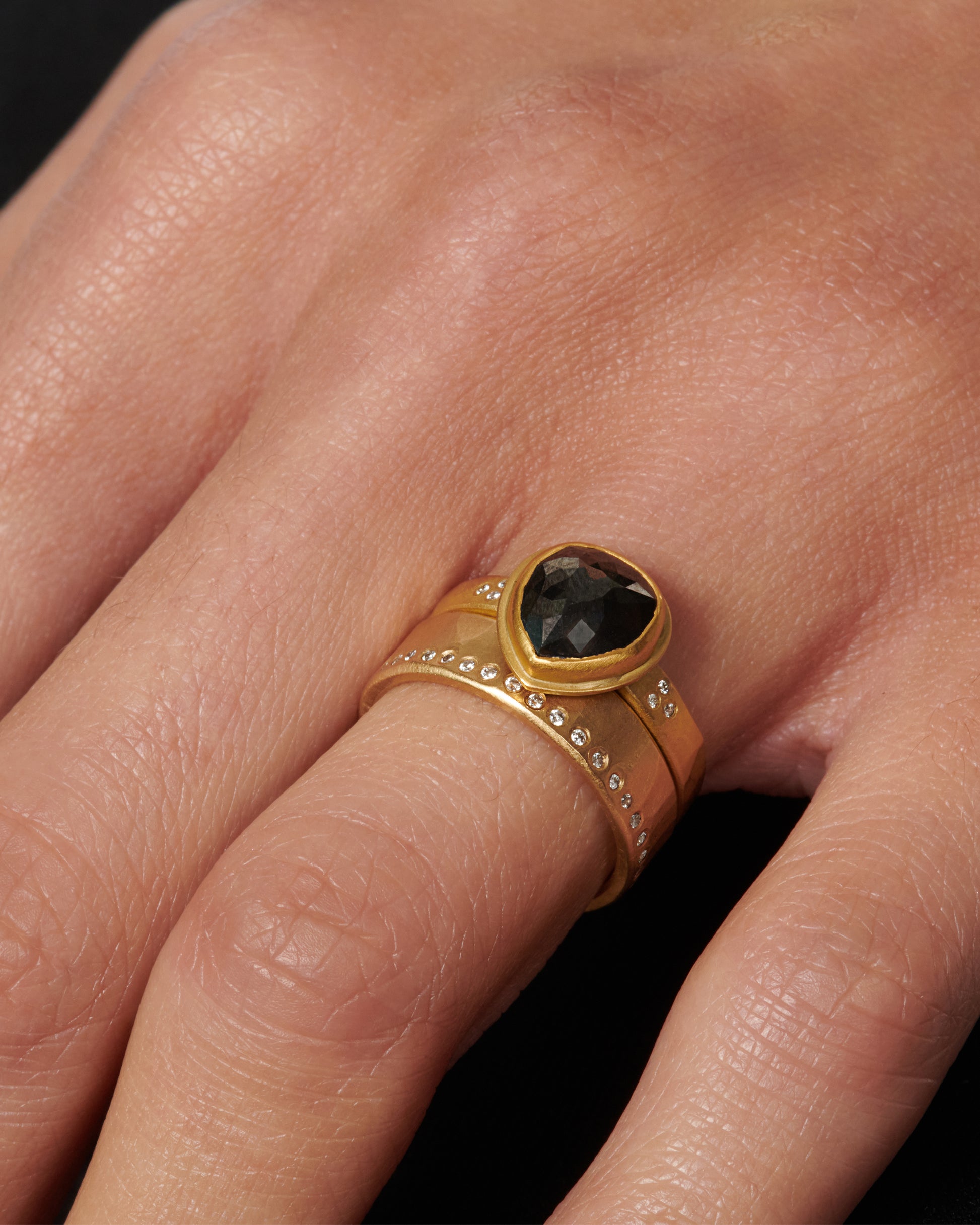 A faceted, pear shaped black diamond in a 22k gold setting with white diamond accents.