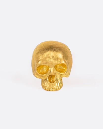 A solid yellow gold skull stud earring. Shown from the front.