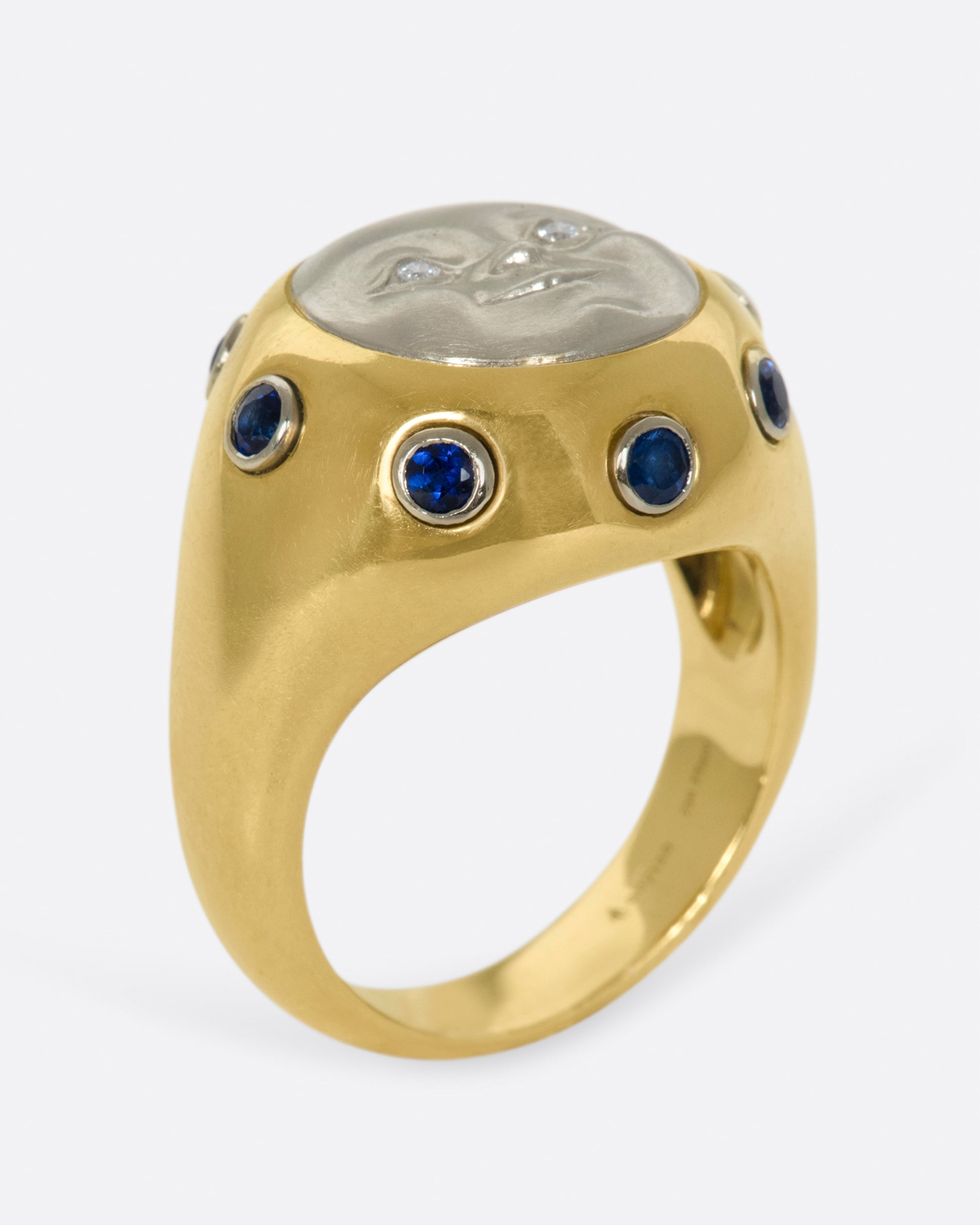 A platinum moonface sunken into a gold ring, surrounded by sapphire cabochons.