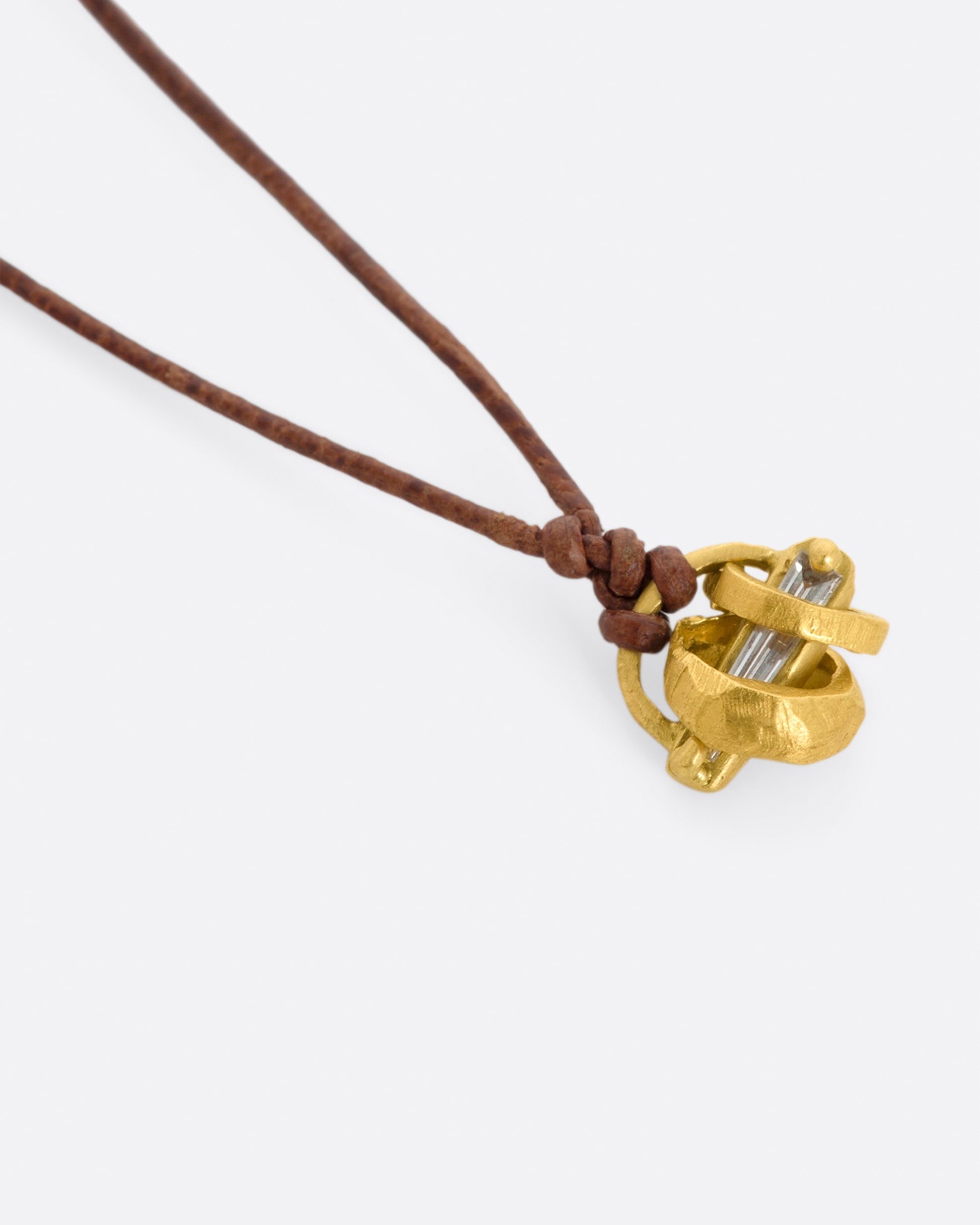 A yellow gold pendant with diamond baguette and yellow gold beads on a leather cord. View laying flat, from the side.