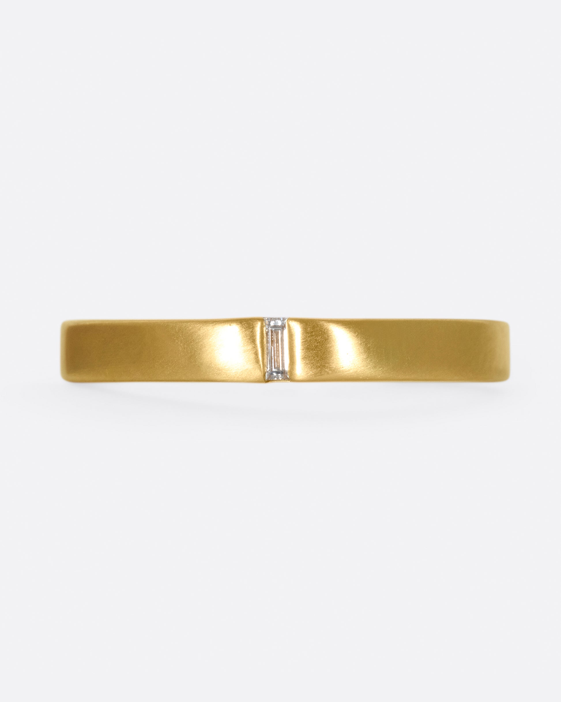 A matte gold band cast in a simple silhouette, featuring one needle baguette-cut diamond for that extra flare.