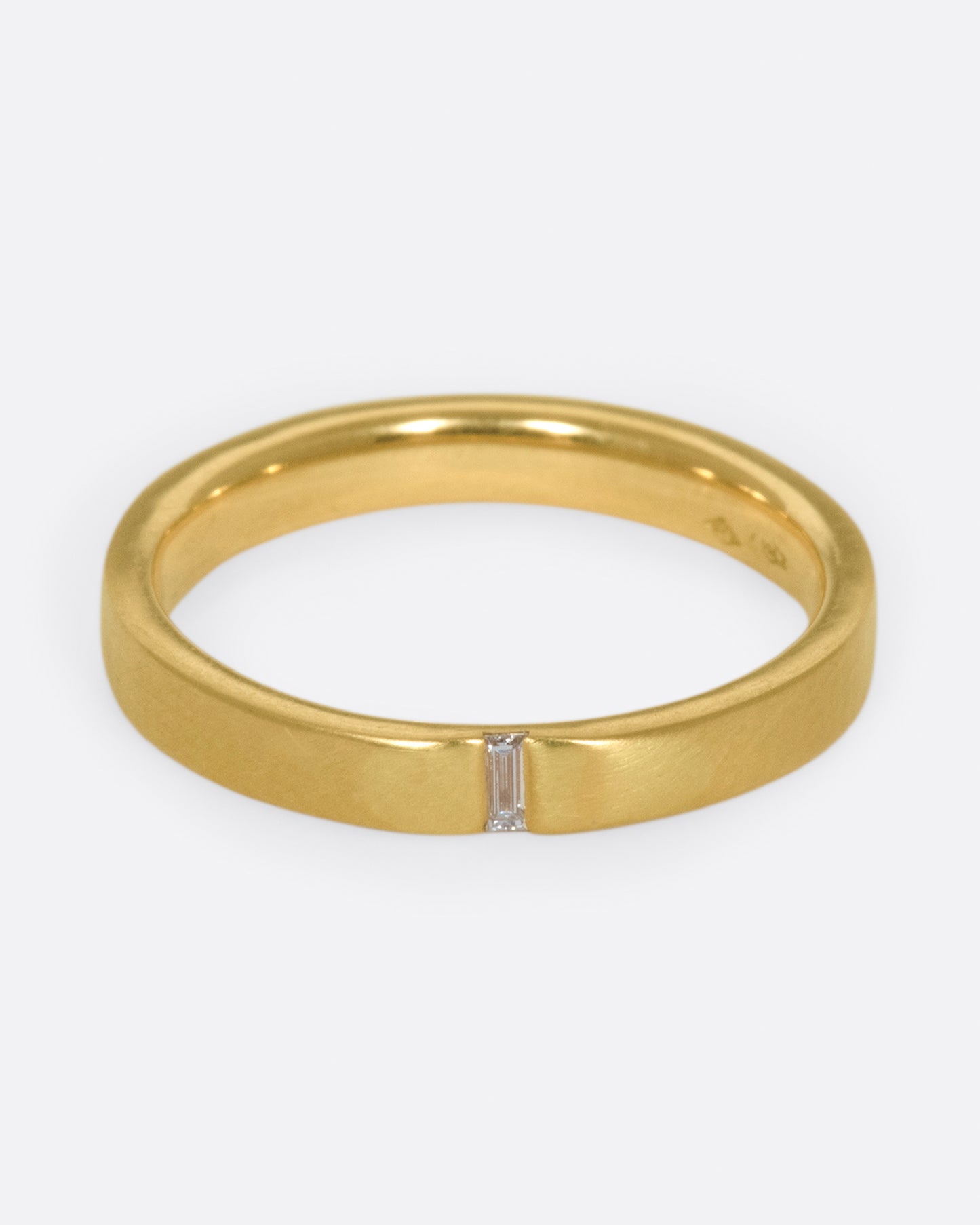 A matte gold band cast in a simple silhouette, featuring one needle baguette-cut diamond for that extra flare.