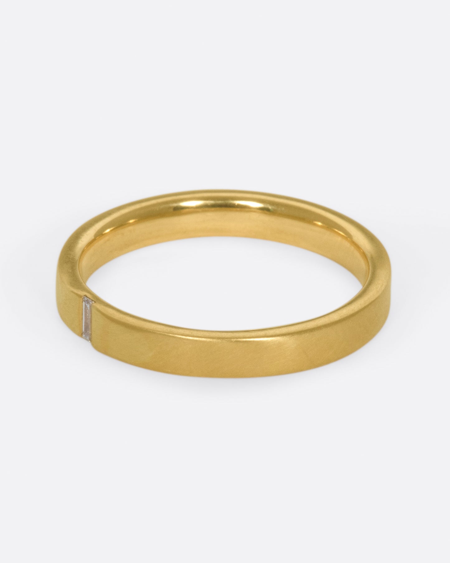 A matte gold band cast in a simple silhouette, featuring one needle baguette-cut diamond for that extra flare.