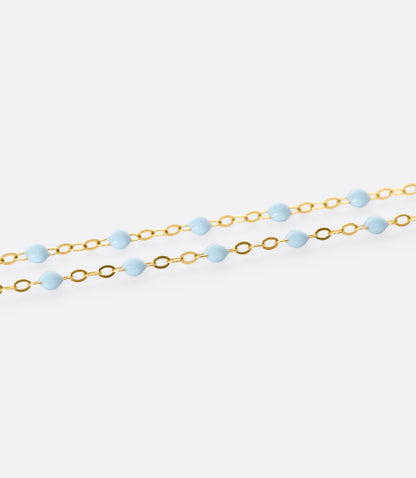 A close up view of a yellow gold cable chain bracelet with baby blue resin droplets. 